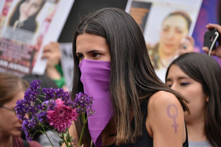 Woman with purple scarf over face holding purple flowers